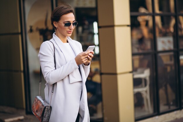 Giovane donna di affari in cappotto per mezzo del telefono