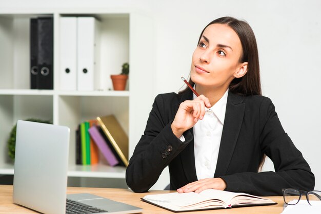 Giovane donna di affari premurosa con il diario e computer portatile sullo scrittorio di legno nell&#39;ufficio