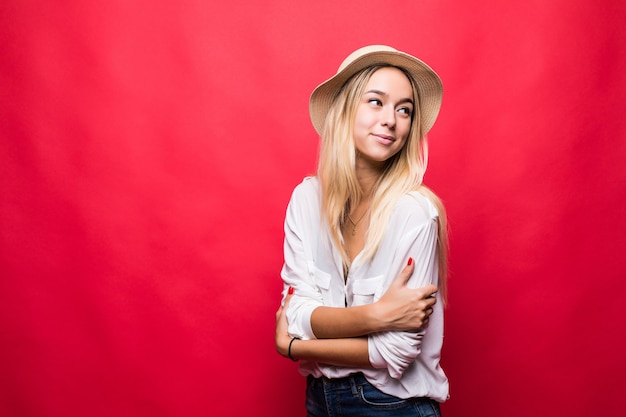 Giovane donna di bellezza che indossa in cappello di paglia con le mani incrociate sorridente isolato sulla parete rossa