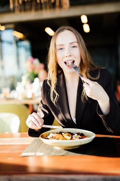 Giovane donna di bellezza che mangia cibo sano seduto nel bellissimo interno con fiori verdi