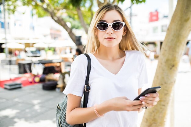 Giovane donna di bellezza utilizzando smart phone all'aperto nella soleggiata strada estiva