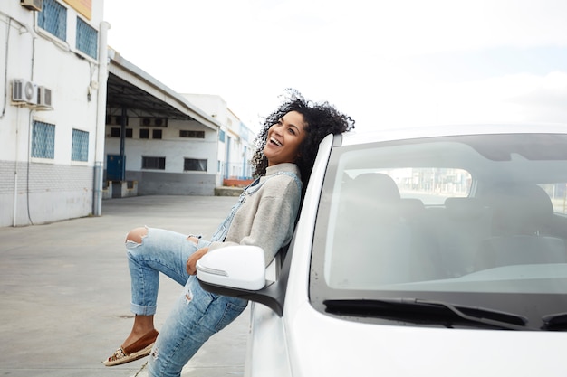 giovane donna di colore con i capelli afro ridendo e godendo appoggiandosi sulla sua auto