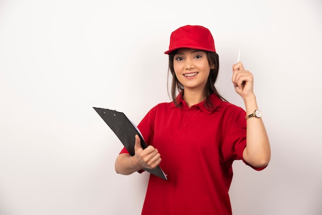 Giovane donna di consegna in uniforme rossa con appunti su sfondo bianco.