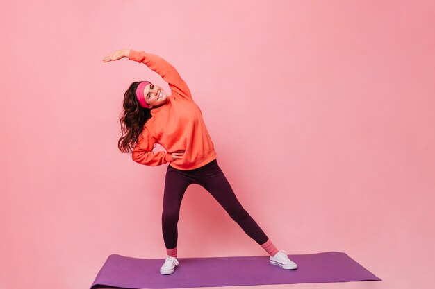 Giovane donna di ottimo umore facendo yoga sul tappetino fitness viola