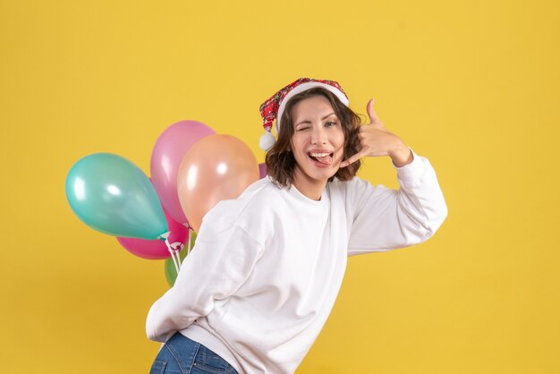 Giovane donna di vista frontale che nasconde i palloncini variopinti sull'emozione gialla della donna di festa di colore di Natale del nuovo anno