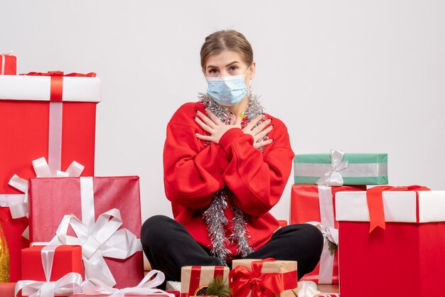 Giovane donna di vista frontale che si siede con i regali di Natale in maschera