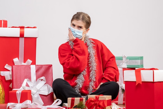 Giovane donna di vista frontale che si siede con i regali di Natale nella mascherina sterile