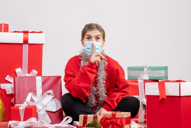 Giovane donna di vista frontale che si siede con i regali di Natale nella mascherina sterile