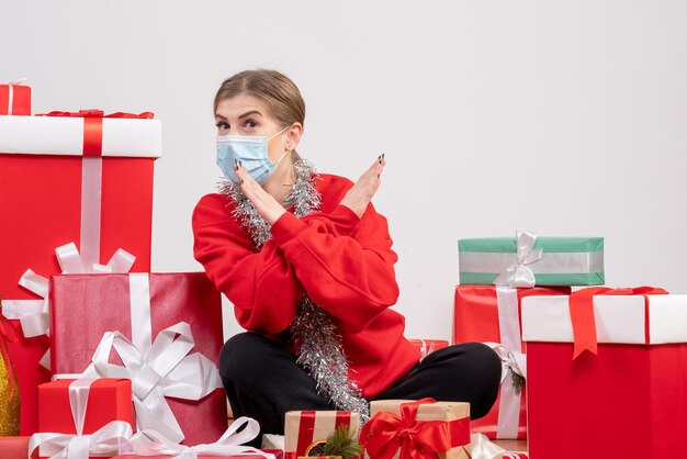 Giovane donna di vista frontale che si siede con i regali di Natale nella mascherina sterile