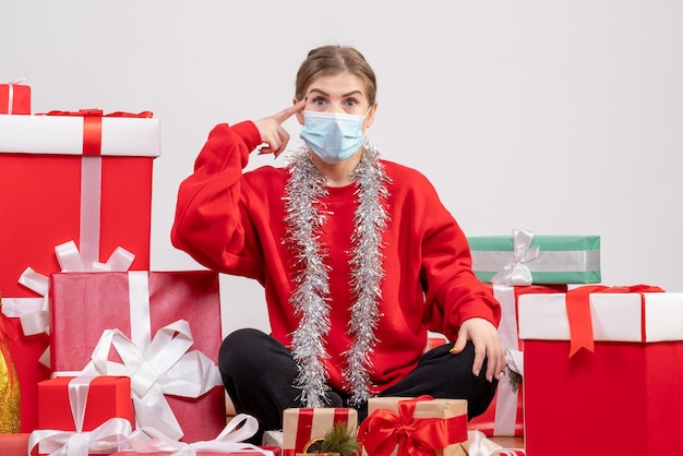 Giovane donna di vista frontale che si siede con i regali di Natale nella mascherina sterile