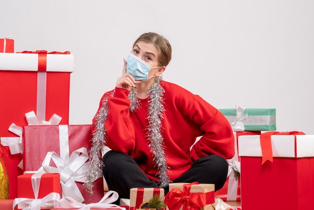 Giovane donna di vista frontale che si siede con i regali di Natale nella mascherina sterile