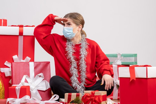 Giovane donna di vista frontale che si siede con i regali di Natale nella mascherina sterile