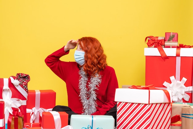 Giovane donna di vista frontale che si siede intorno ai regali di natale nella maschera su colore giallo