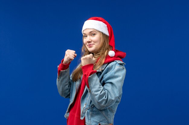 Giovane donna di vista frontale che sorride e che mostra i suoi pugni sul colore blu di emozione di natale del fondo