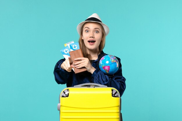 Giovane donna di vista frontale che tiene i biglietti e il globo sul viaggio di vacanza del mare di viaggio aereo del fondo blu-chiaro