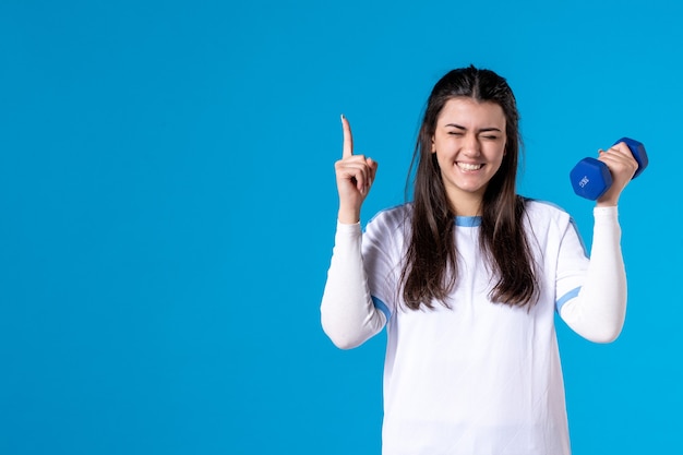 Giovane donna di vista frontale che tiene i manubri blu sulla parete blu