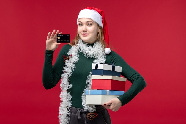 Giovane donna di vista frontale che tiene i regali del nuovo anno su fondo rosso
