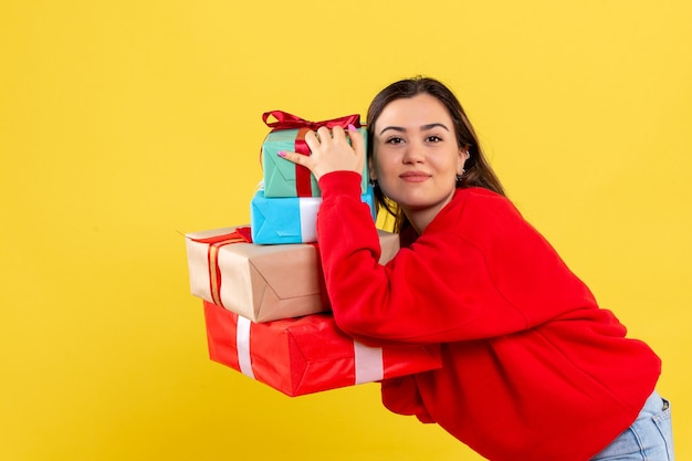 Giovane donna di vista frontale che tiene i regali di natale su fondo giallo