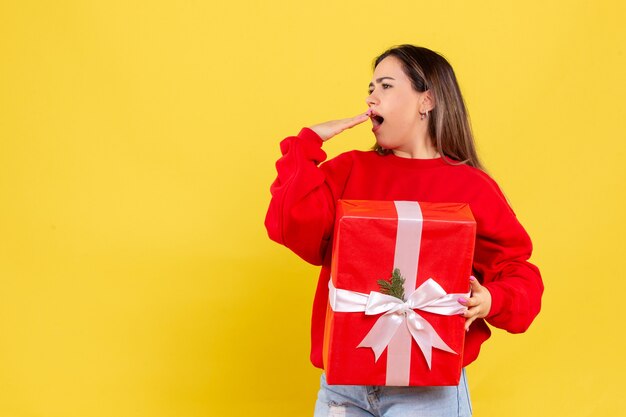 Giovane donna di vista frontale che tiene il regalo di natale su fondo giallo