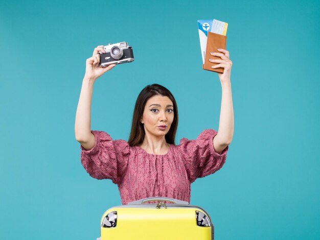 Giovane donna di vista frontale che va in macchina fotografica della tenuta di vacanza e biglietti sul mare della donna di vacanza di viaggio del fondo blu all'estero