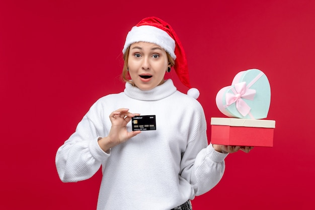 Giovane donna di vista frontale con regali e carta di credito sullo scrittorio rosso