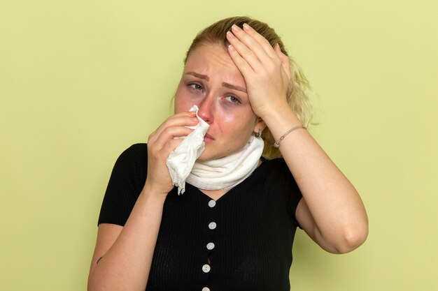 Giovane donna di vista frontale con un asciugamano bianco intorno alla gola che si sente molto malato e malato pulendosi il naso sulla ragazza di salute femminile