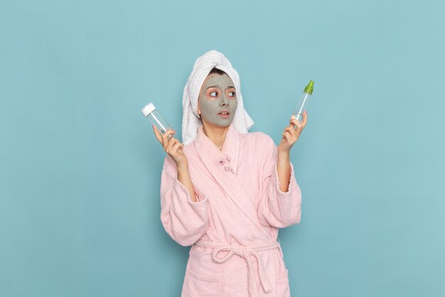 Giovane donna di vista frontale in accappatoio rosa dopo la doccia che tiene gli spruzzi sulla parete blu chiaro bellezza acqua crema selfcare doccia bagno