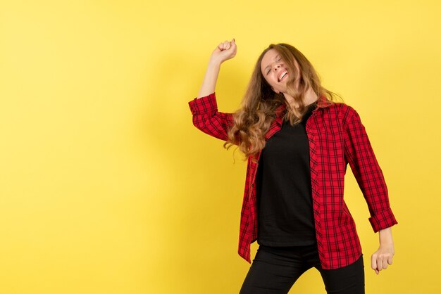 Giovane donna di vista frontale in camicia a scacchi rossa che balla su un'emozione di donna di modello di colore umano sfondo giallo