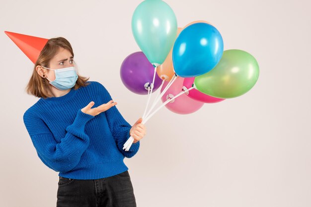 Giovane donna di vista frontale in maschera che tiene palloncini colorati