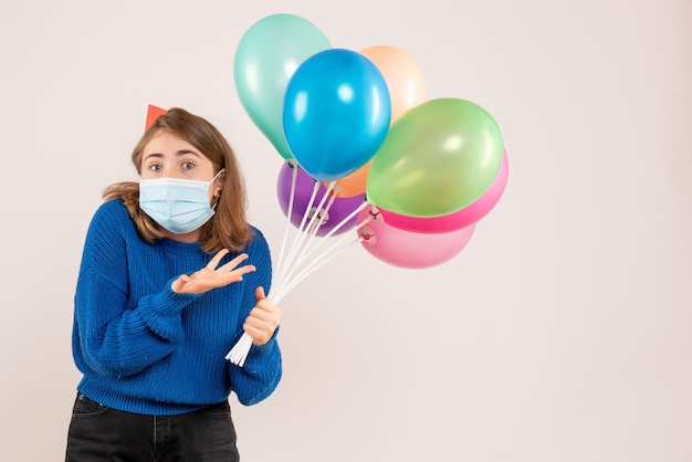 Giovane donna di vista frontale in maschera che tiene palloncini colorati