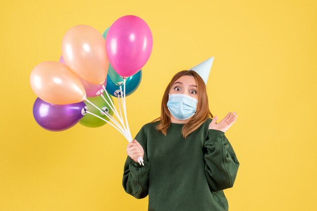 Giovane donna di vista frontale in maschera che tiene palloncini colorati