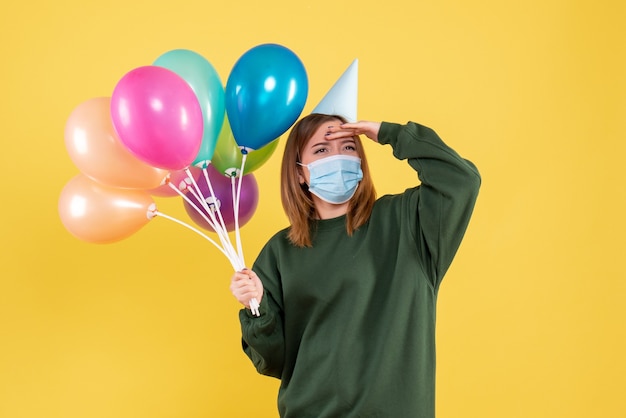 Giovane donna di vista frontale in maschera che tiene palloncini colorati