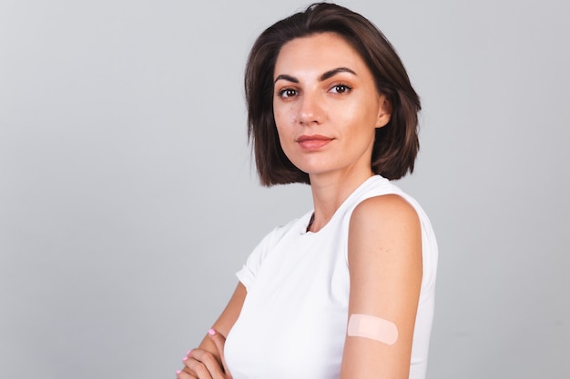 Giovane donna dopo la vaccinazione che mostra braccio con bendaggio in gesso. Protezione dal virus. COVID-2019.