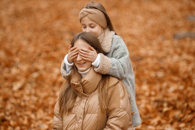 Giovane donna e bambina nella foresta autunnale Bambina chiude gli occhi di una madre con le mani Ragazza che indossa una giacca grigia alla moda e una donna marrone