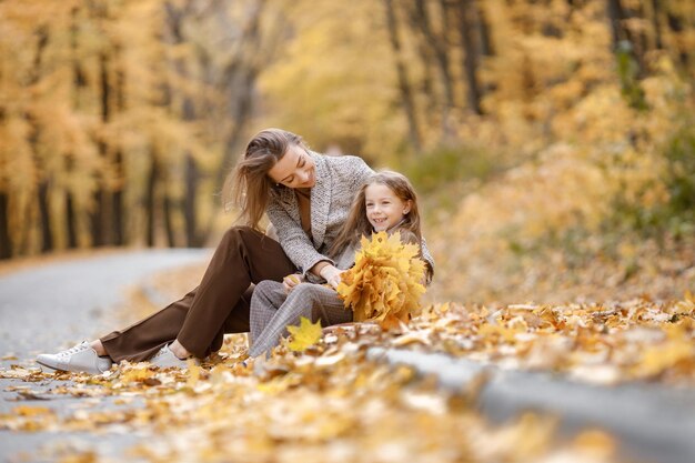 Giovane donna e bambina nella foresta di autunno. Donna seduta vicino a sua figlia che tiene in mano foglie gialle. Madre che abbraccia sua figlia.
