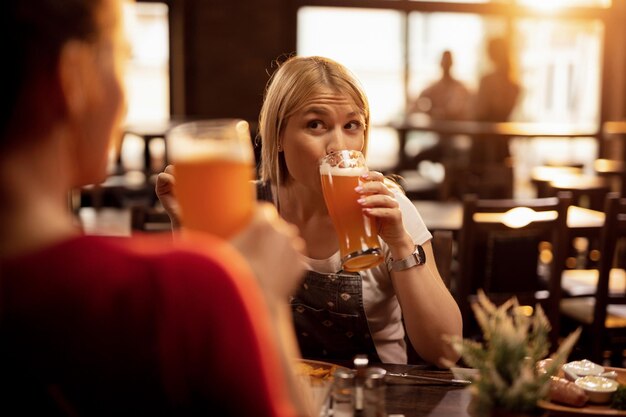 Giovane donna e la sua amica che bevono birra e si godono un pranzo al ristorante