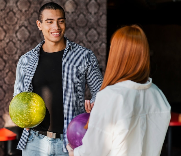 Giovane donna ed uomo che tengono il colpo medio delle palle da bowling variopinte