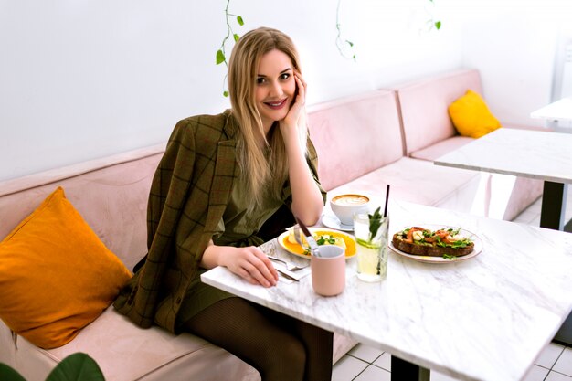 Giovane donna elegante alla moda che gode della sua gustosa colazione al caffè alla moda hipster, mattina, vestito elegante.