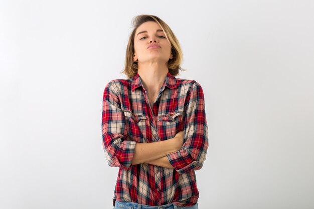 Giovane donna emotiva abbastanza divertente in camicia a scacchi in posa isolato sulla parete bianca dello studio, mostrando il gesto arrabbiato