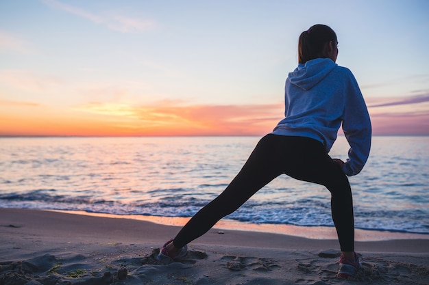 Giovane donna facendo esercizi sportivi sulla spiaggia di alba al mattino