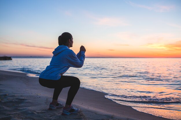 Giovane donna facendo esercizi sportivi sulla spiaggia di alba al mattino