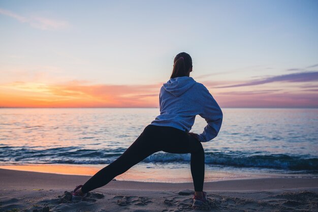 Giovane donna facendo esercizi sportivi sulla spiaggia di alba al mattino