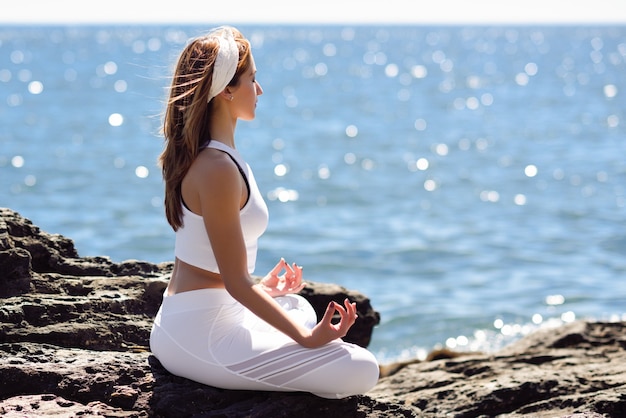 Giovane donna facendo yoga in spiaggia indossando abiti bianchi