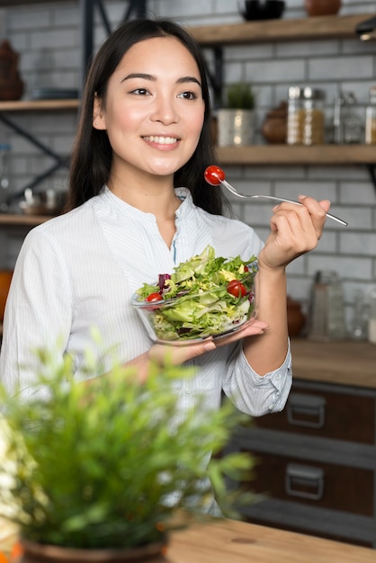 Giovane donna felice asiatica che mangia insalata verde sana