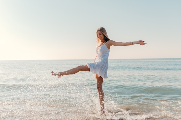 Giovane donna felice che balla girando da mare spiaggia soleggiata estate moda stile in vacanza vestito bianco