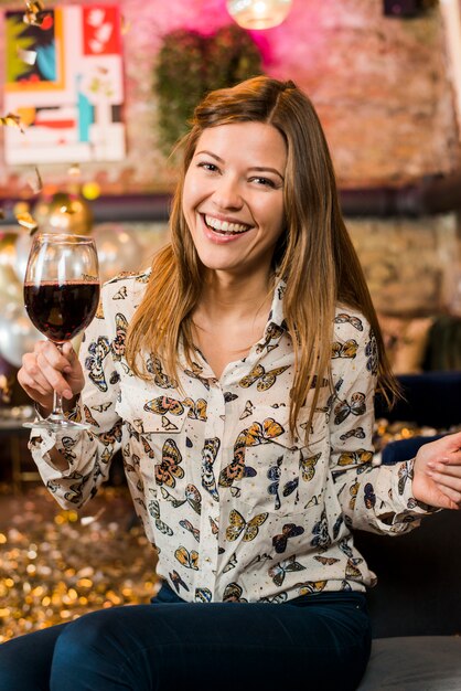 Giovane donna felice che gode del partito che tiene il vetro di vino