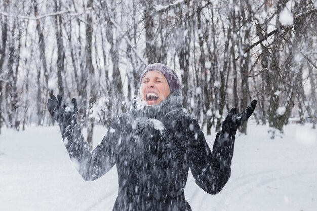 Giovane donna felice che gode delle precipitazioni nevose alla foresta di inverno