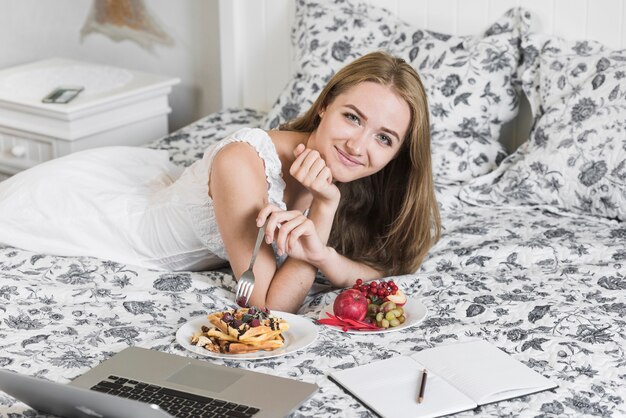 Giovane donna felice che si distende sulla base che mangia prima colazione sana