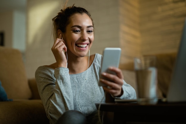 Giovane donna felice che si diverte mentre utilizza il telefono cellulare e legge un messaggio di testo nel suo soggiorno