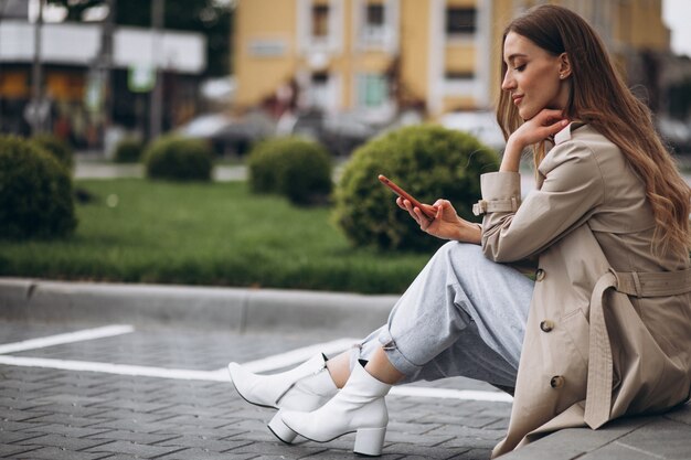 Giovane donna felice che si siede nel parco e che parla al telefono